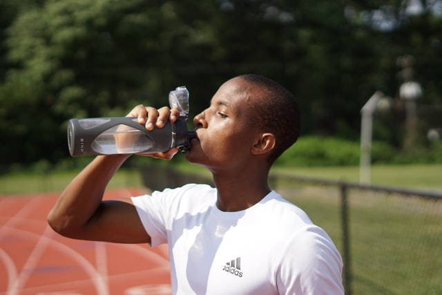 man drinking water in field and track